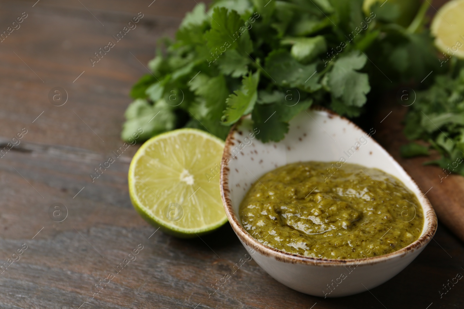 Tasty sauce with cilantro and lime on wooden table, closeup. Space for text Photo of Tasty sauce with cilantro and lime on wooden table, closeup. Space for text