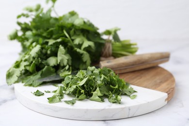 Photo of Fresh green cilantro and knife on white marble table, closeup