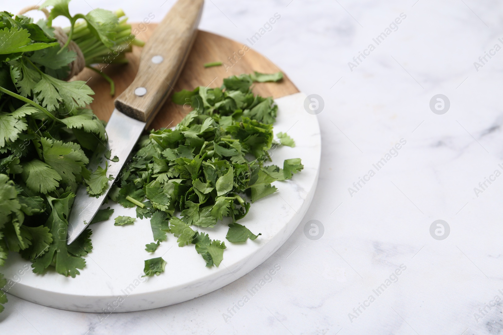Photo of Fresh green cilantro and knife on white marble table, closeup. Space for text