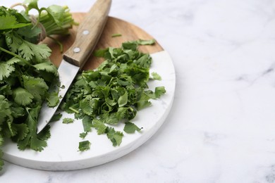 Photo of Fresh green cilantro and knife on white marble table, closeup. Space for text