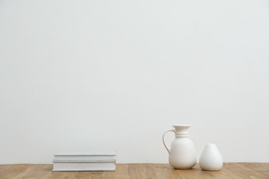 Photo of Different vases and books on wooden table near white wall indoors