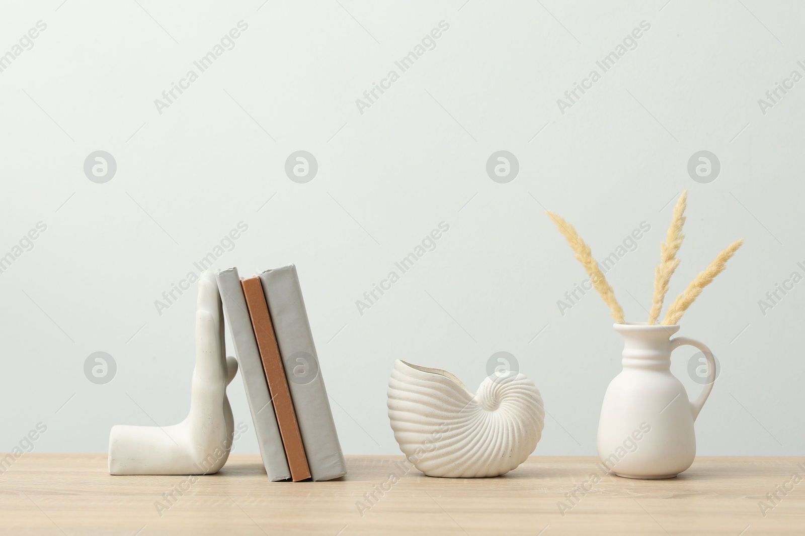 Different decor and books on wooden table near white wall indoors Photo of Different decor and books on wooden table near white wall indoors