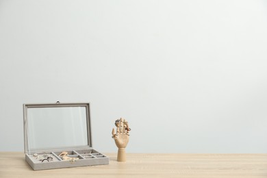 Photo of Jewelry box with many different accessories and mannequin hand on wooden table near white wall indoors, space for text