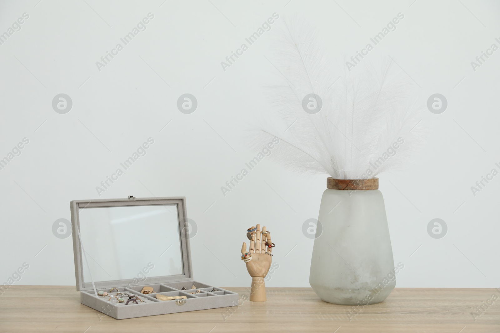 Jewelry box with many different accessories, mannequin hand and other decor on wooden table near white wall indoors Photo of Jewelry box with many different accessories, mannequin hand and other decor on wooden table near white wall indoors