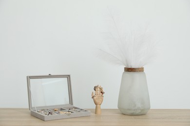 Photo of Jewelry box with many different accessories, mannequin hand and other decor on wooden table near white wall indoors