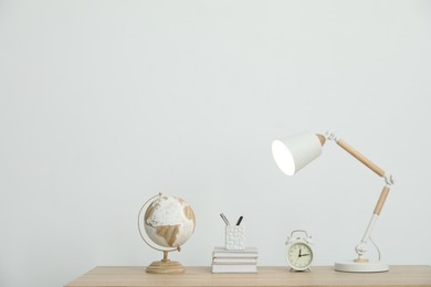 Photo of Lamp, books, stationery, alarm clock and globe on wooden table near white wall indoors