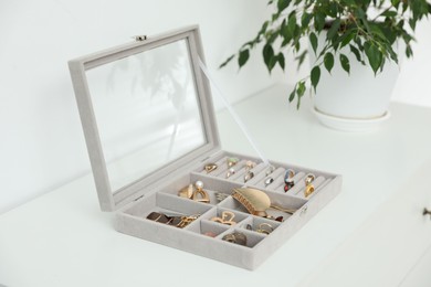 Photo of Jewelry box with many different accessories and green houseplant on white cabinet indoors, closeup