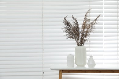 Photo of Dried reeds and vases on white table near window indoors, space for text