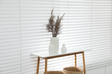 Photo of Dried reeds and vases on white table near window indoors