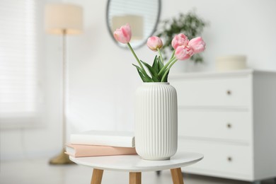 Photo of Beautiful tulip flowers in vase and books on white table indoors