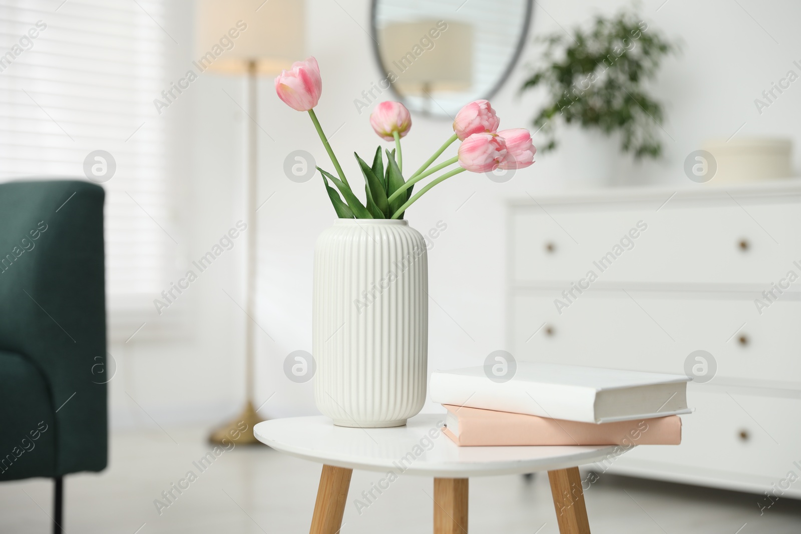 Beautiful tulip flowers in vase and books on white table indoors Photo of Beautiful tulip flowers in vase and books on white table indoors