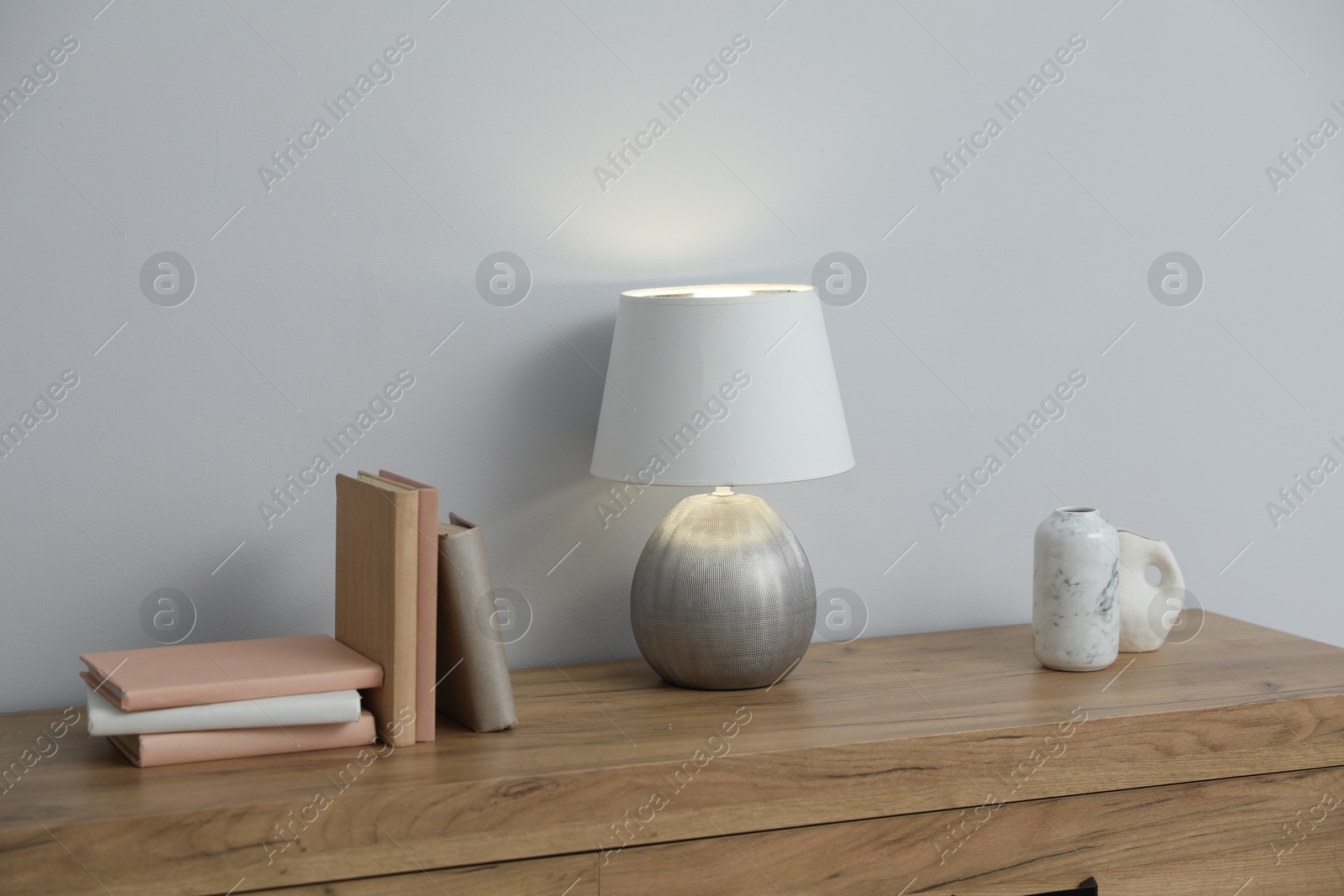 Lamp, books and vases on wooden cabinet near white wall indoors Photo of Lamp, books and vases on wooden cabinet near white wall indoors
