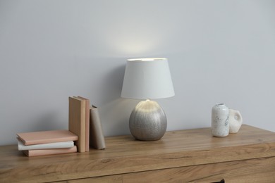 Photo of Lamp, books and vases on wooden cabinet near white wall indoors
