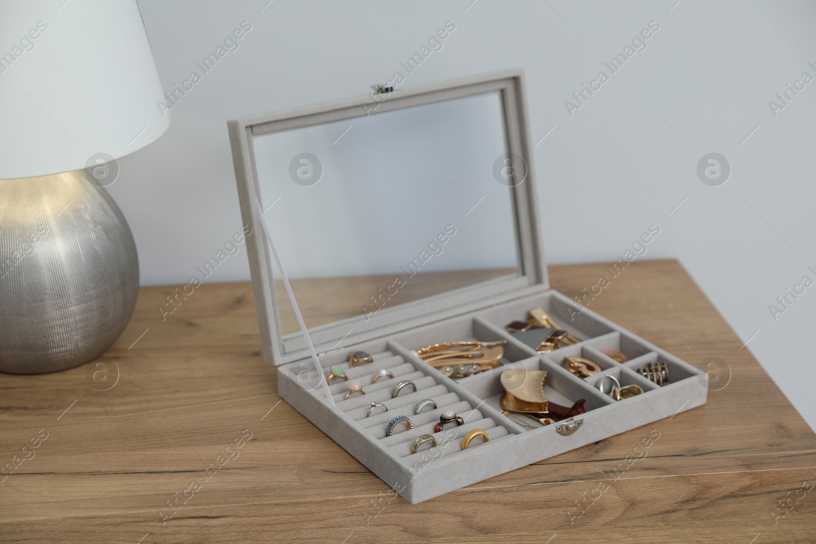 Jewelry box with many different accessories and lamp on wooden table near white wall indoors, closeup Photo of Jewelry box with many different accessories and lamp on wooden table near white wall indoors, closeup