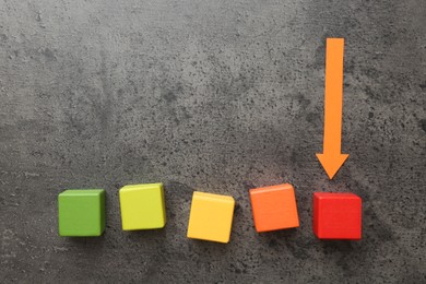 Photo of Maximum. Colorful cubes and arrow pointing at red one on grey table, flat lay