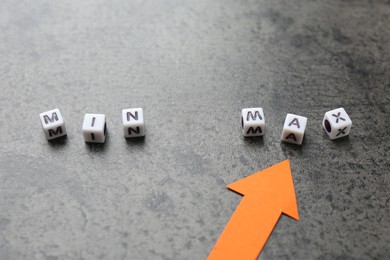Photo of Words Min and Max made of cubes with arrow pointing at it on grey table, closeup