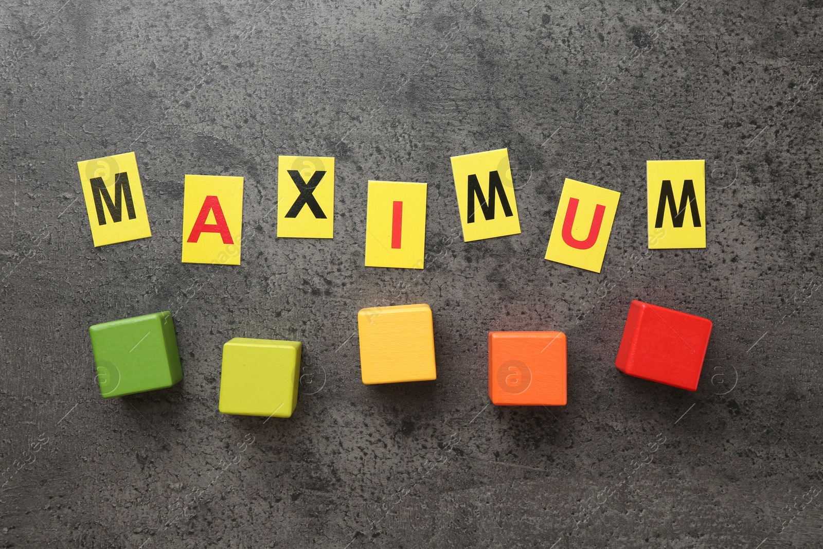 Word Maximum and colorful cubes on grey table, flat lay Photo of Word Maximum and colorful cubes on grey table, flat lay