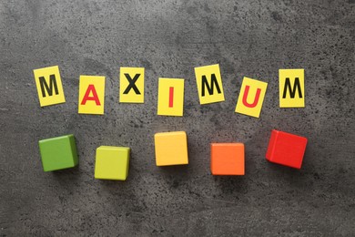 Photo of Word Maximum and colorful cubes on grey table, flat lay