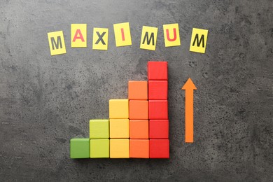 Photo of Word Maximum, arrow and colorful cubes on grey table, flat lay