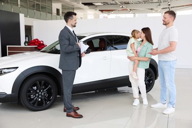 Photo of Salesman with clipboard showing new car to happy family in salon