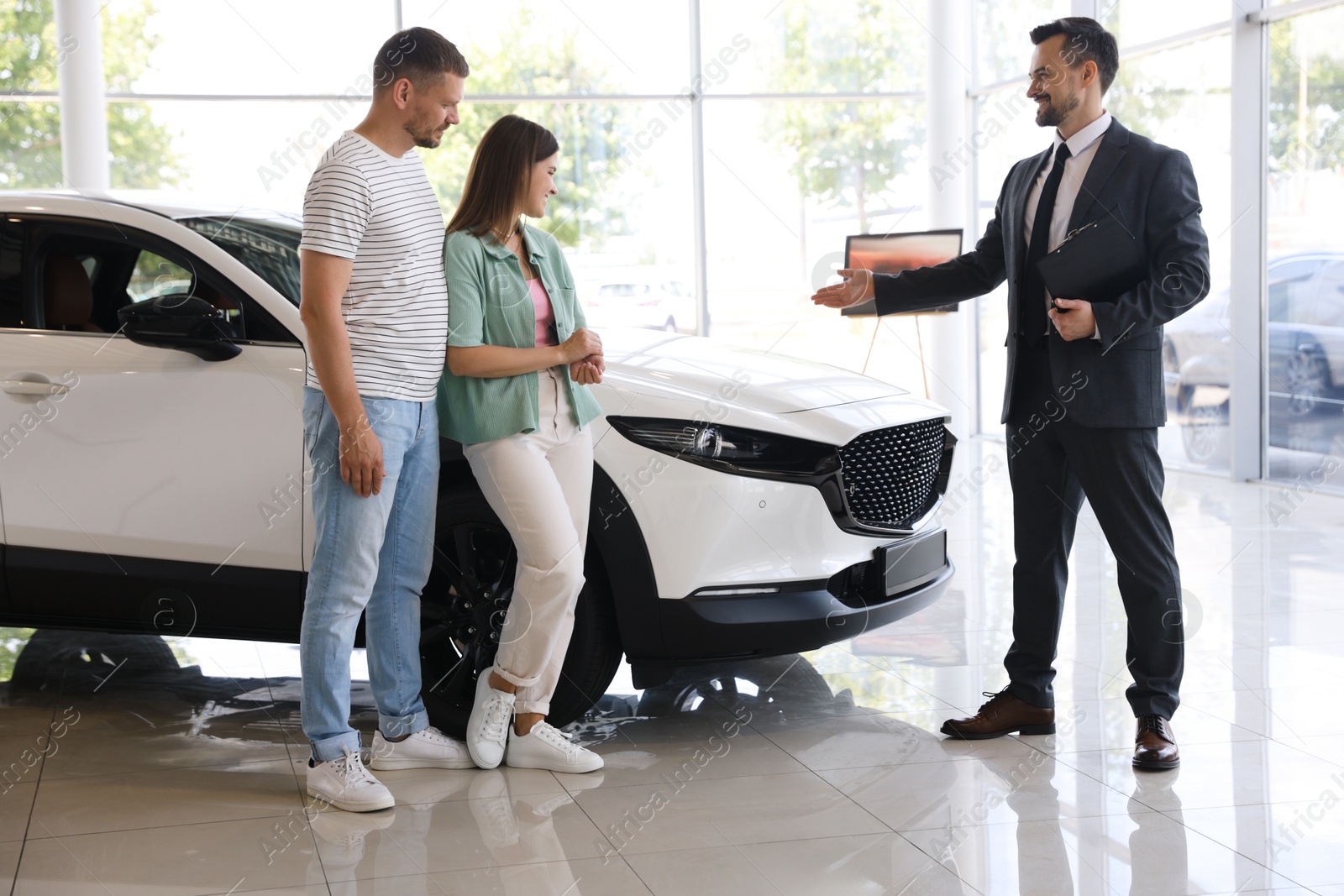 Photo of Salesman with clipboard showing new car to happy family in salon