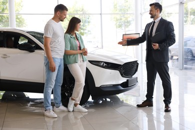 Photo of Salesman with clipboard showing new car to happy family in salon