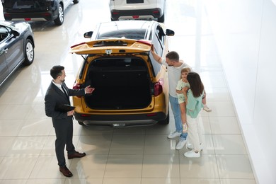 Photo of Salesman with clipboard showing new car to happy family in salon