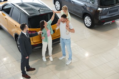 Photo of Salesman giving car key to happy family in salon