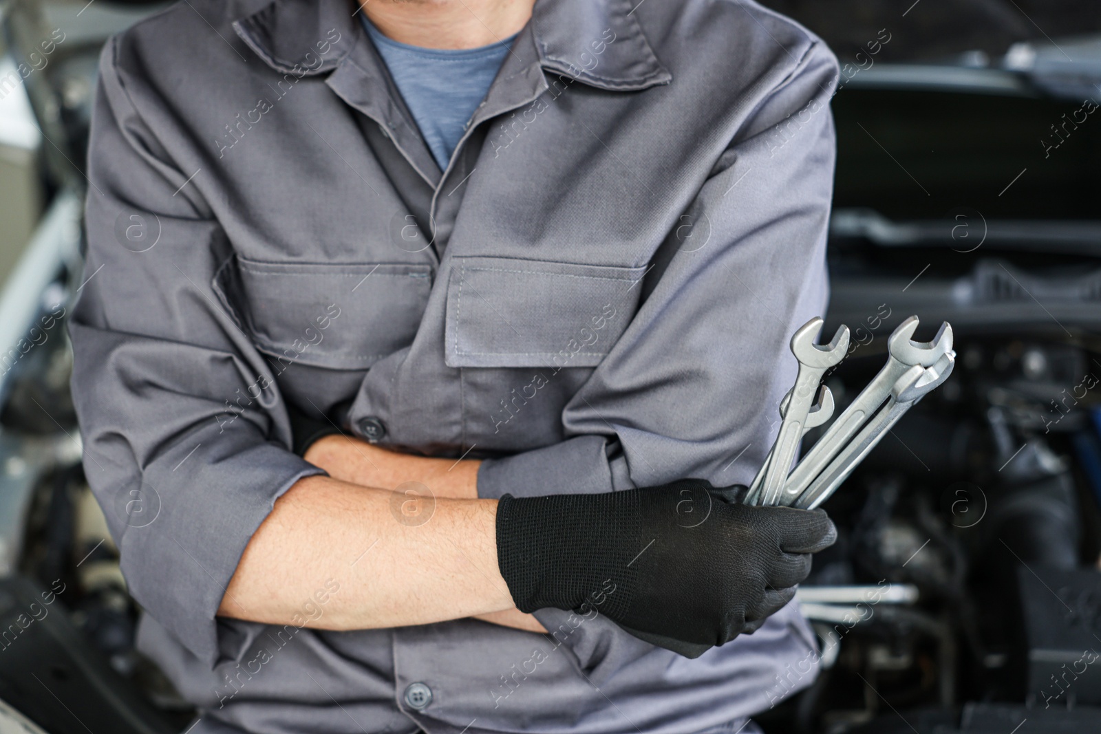 Auto parts. Professional mechanic with different wrenches near open hood of car indoors, closeup Photo of Auto parts. Professional mechanic with different wrenches near open hood of car indoors, closeup