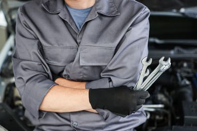 Photo of Auto parts. Professional mechanic with different wrenches near open hood of car indoors, closeup