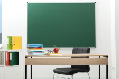 Photo of Different books, glasses and red apple on wooden table near blackboard indoors