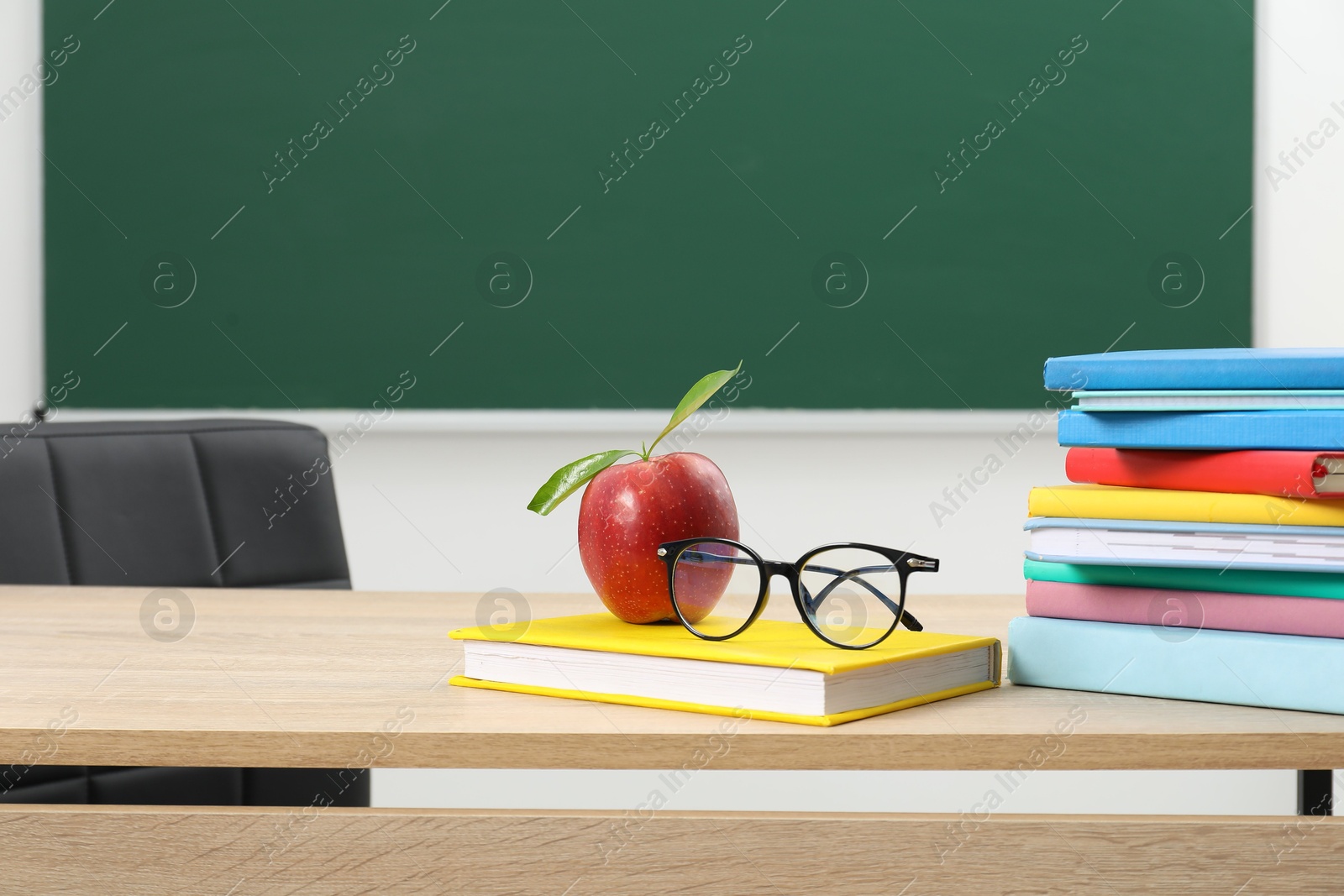 Different books, glasses and red apple on wooden table near blackboard indoors, space for text Photo of Different books, glasses and red apple on wooden table near blackboard indoors, space for text