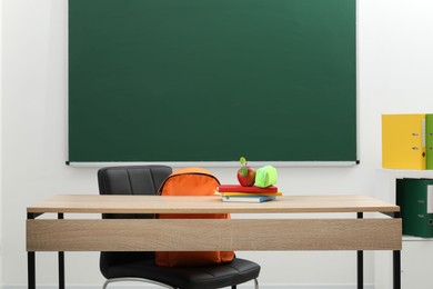 Photo of Different stationery and apple on wooden table near blackboard indoors