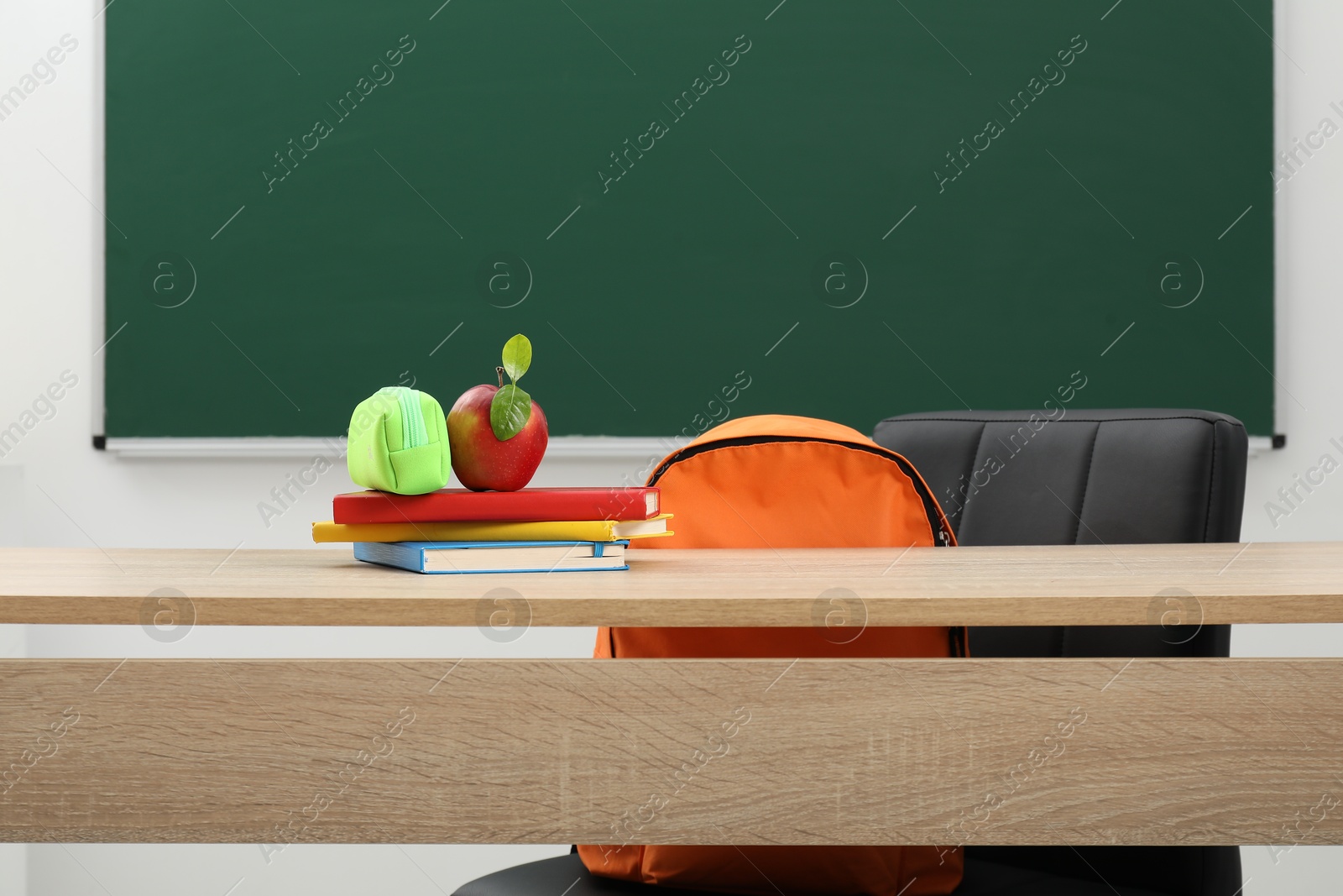 Different stationery and apple on wooden table near blackboard indoors Photo of Different stationery and apple on wooden table near blackboard indoors