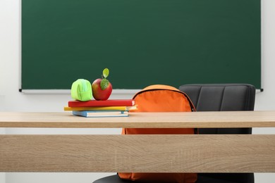 Photo of Different stationery and apple on wooden table near blackboard indoors
