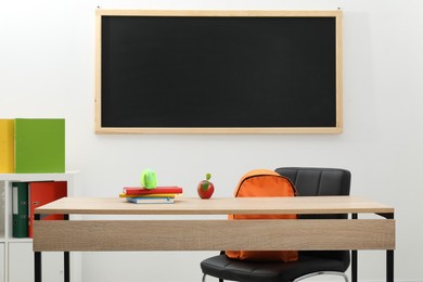 Photo of Different stationery and red apple on wooden table near blackboard indoors