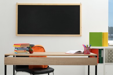 Photo of Different stationery and red apple on wooden table near blackboard indoors
