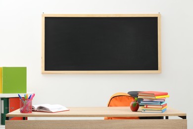 Photo of Different stationery and red apple on wooden table near blackboard indoors