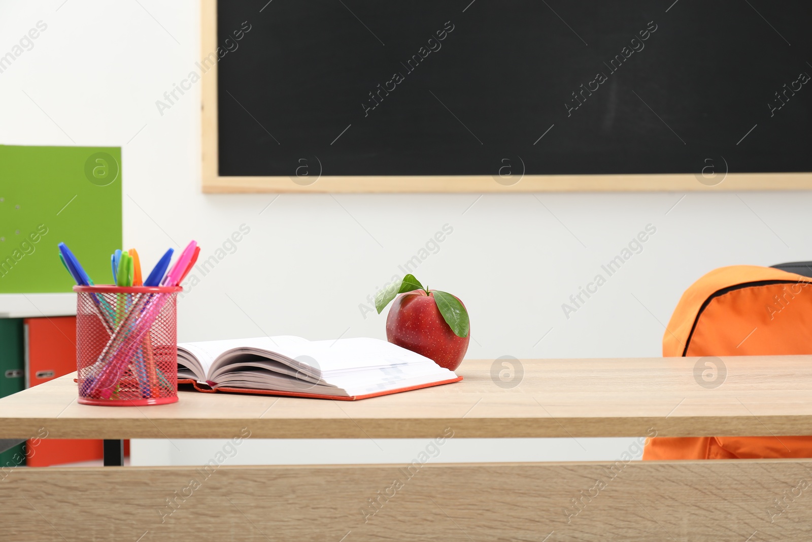 Different stationery and red apple on wooden table near blackboard indoors Photo of Different stationery and red apple on wooden table near blackboard indoors