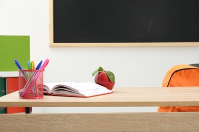 Photo of Different stationery and red apple on wooden table near blackboard indoors