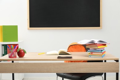 Photo of Different stationery and red apple on wooden table near blackboard indoors
