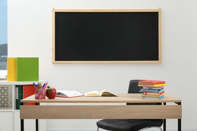 Photo of Different stationery and red apple on wooden table near blackboard indoors