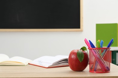 Photo of Different stationery and red apple on wooden table near blackboard indoors