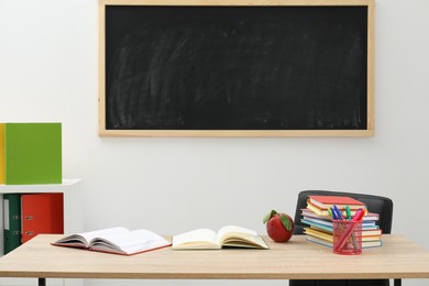 Photo of Different stationery and red apple on wooden table near blackboard indoors