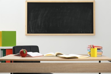 Photo of Different stationery and red apple on wooden table near blackboard indoors