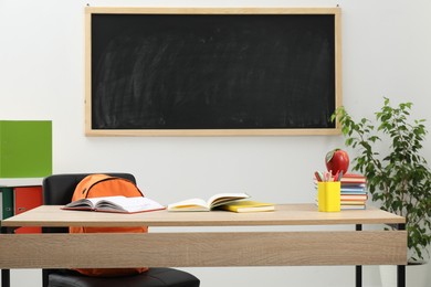 Photo of Different stationery and red apple on wooden table near blackboard indoors