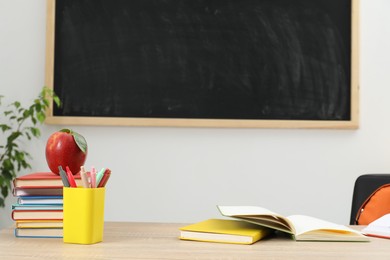 Photo of Different stationery and red apple on wooden table near blackboard indoors