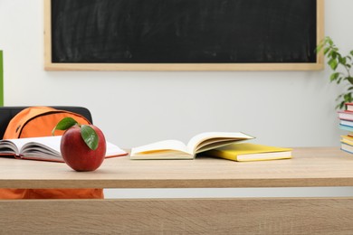 Photo of Different books and red apple on wooden table near blackboard indoors