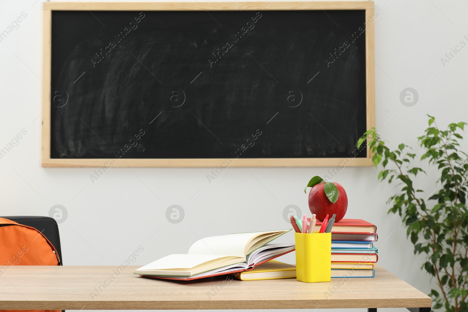 Different stationery and red apple on wooden table near blackboard indoors Photo of Different stationery and red apple on wooden table near blackboard indoors