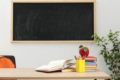 Photo of Different stationery and red apple on wooden table near blackboard indoors